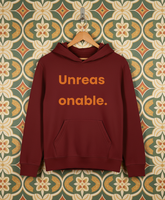 Maroon hoodie with 'Unreas onable.' text on a patterned wall background