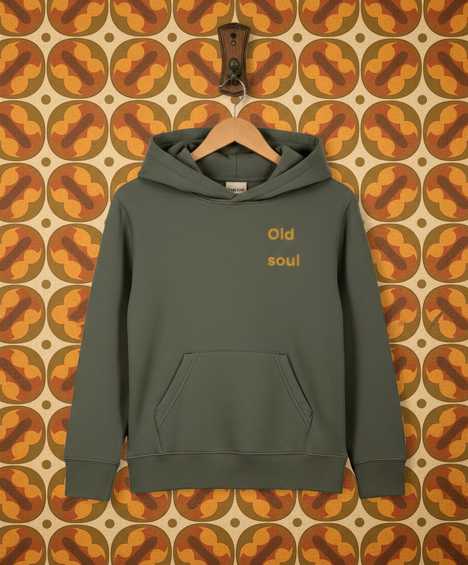 Green hoodie with 'Old soul' text on a hanger against a patterned wall.