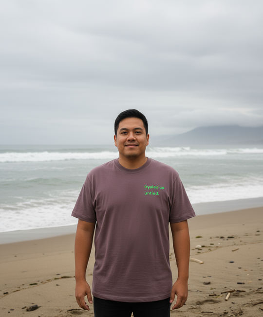 Man standing on a beach wearing a purple t-shirt with text.