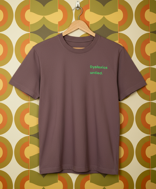 Brown t-shirt with 'Dyslexics untied.' text on a hanger against a patterned wall.