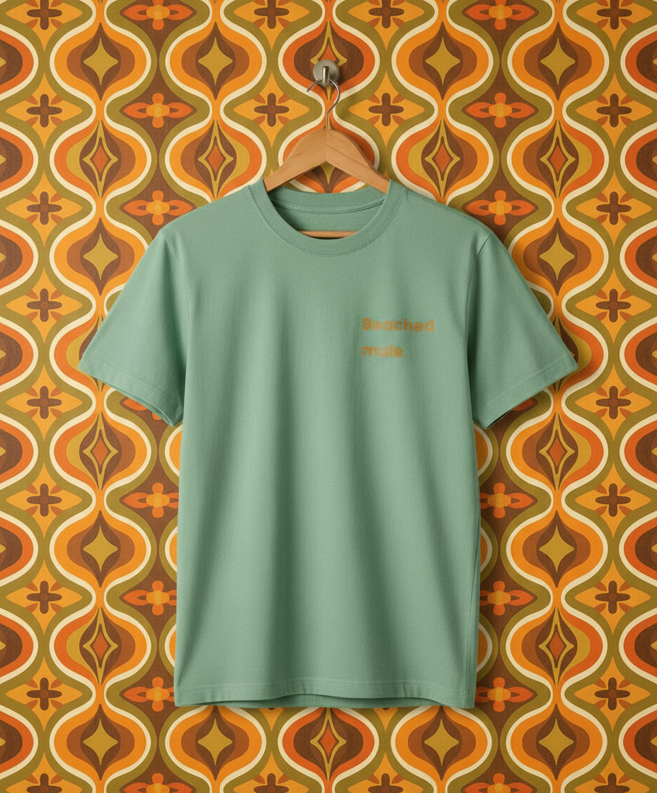 Green t-shirt with text on a hanger against a patterned wall.