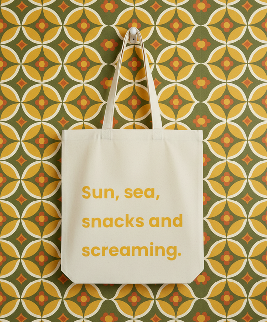 Beige tote bag with 'Sun, sea, snacks and screaming' text on a patterned wall background
