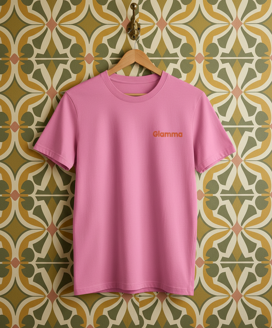 Pink t-shirt with 'Glamma' logo on a hanger against a patterned wall.
