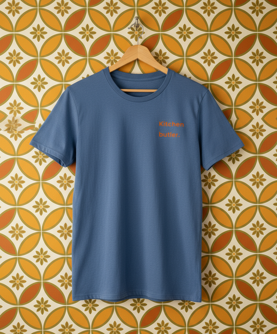 Blue t-shirt with red text on a hanger against a patterned wall.