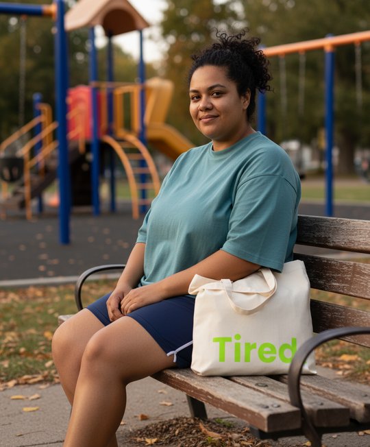 Woman sitting on a bench with a 'Tired' bag at a playground