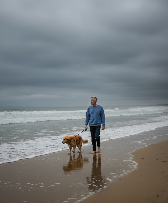 Man walking a dog on a beach with a cloudy sky