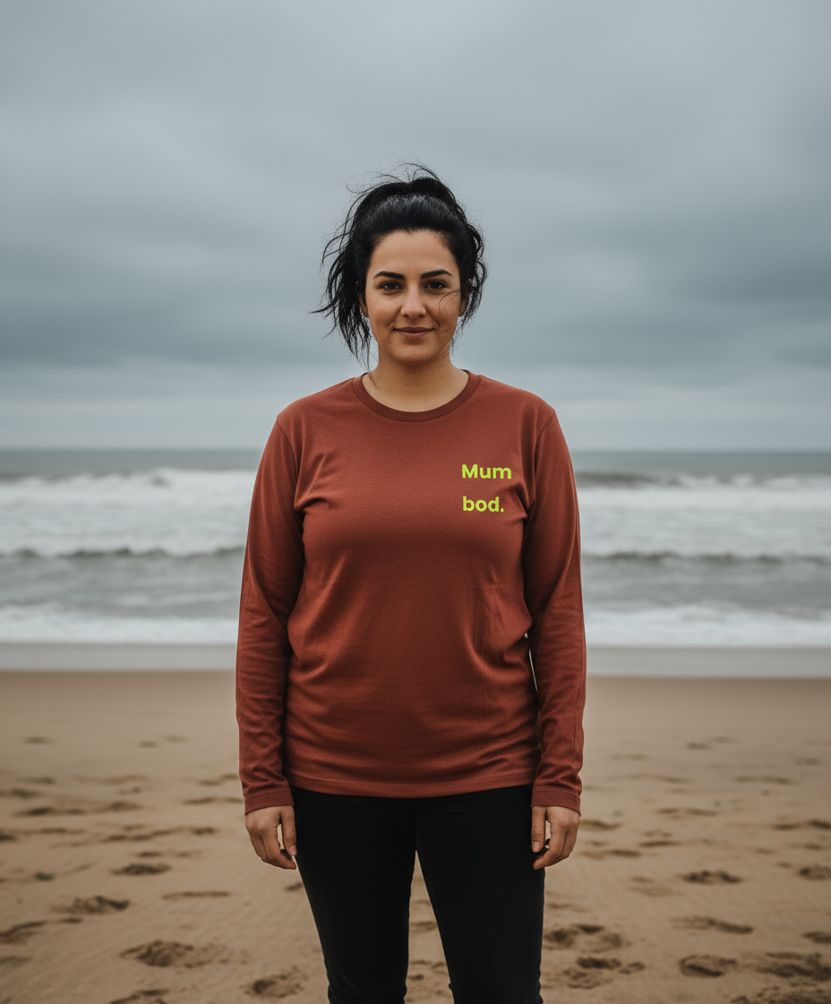 Woman wearing a brown long-sleeve shirt with 'Mum bod.' text on a beach