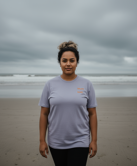 Person wearing a light purple t-shirt on a beach with a cloudy sky