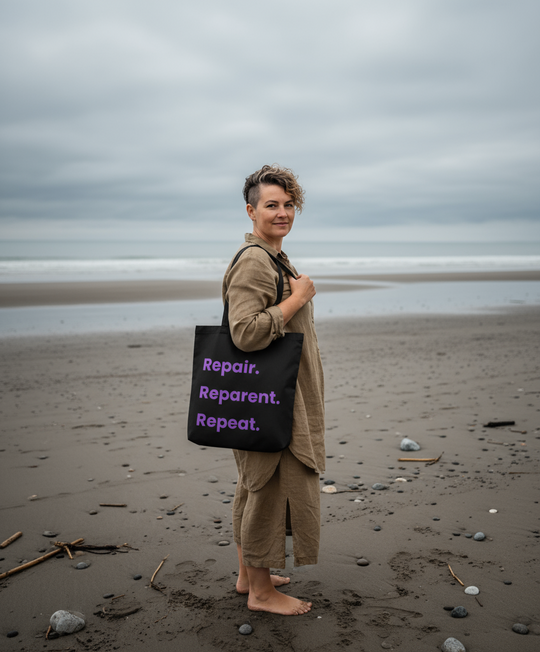 Person standing on a beach holding a black tote bag with purple text.
