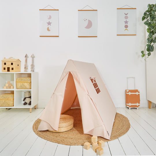 Children's play tent in pink colour, made from cotton canvas, placed in a room with decorative items, toys, and a carrying case visible in the background.