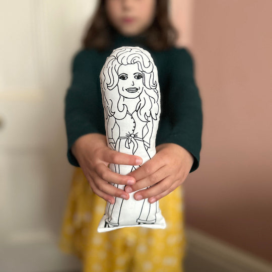 A child holding a black and white screen printed cushion doll depicting Dolly Parton.