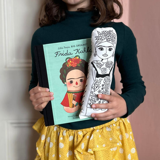 A child holding screen printed doll cushion of Frida Kahlo and also a Little People Big Dreams book about Frida Kahlo's life