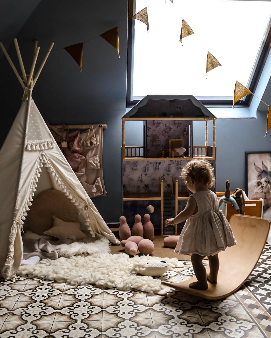 Child playing in a playroom with a teepee, wooden balance board and toys.