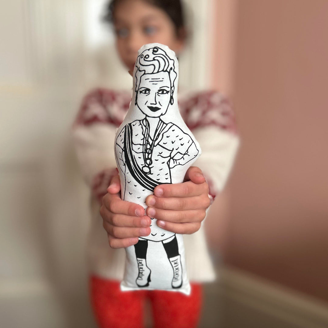 A child holding out the screen printed doll of Vivienne Westwood towards the camera with a blurred background