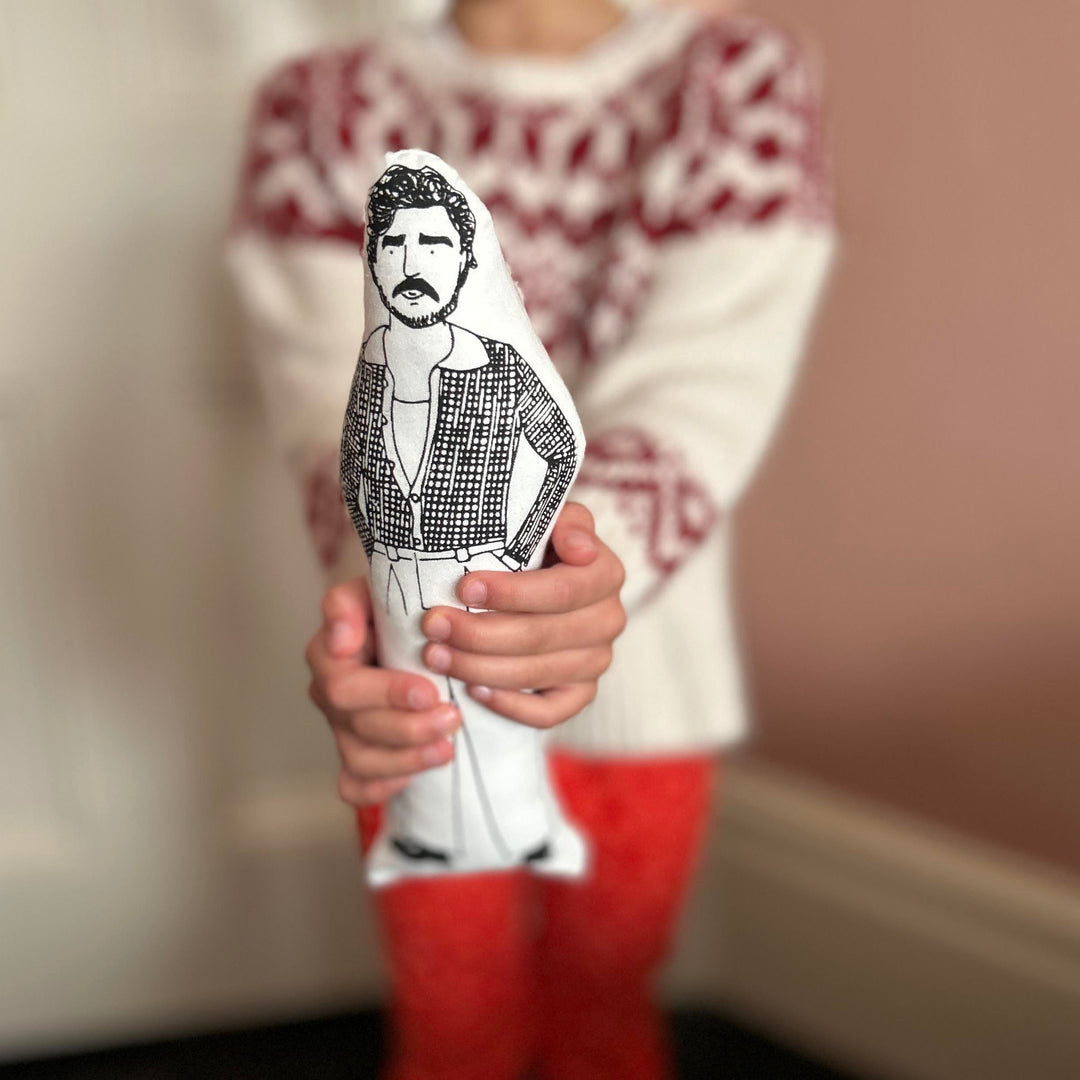 A child holding a black and white screen printed cushion doll depicting an illustration of Pedro Pascal.