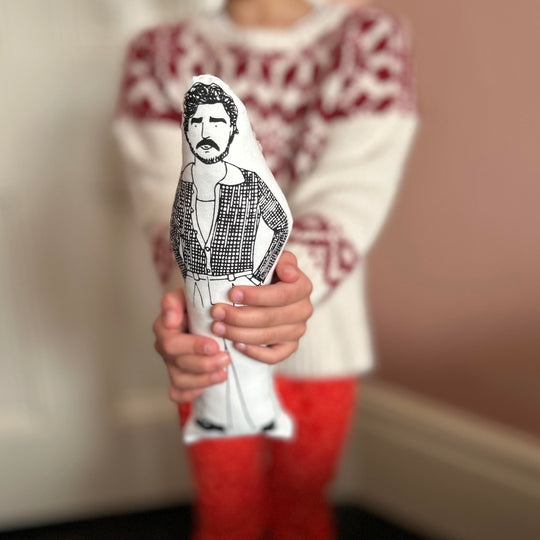 A child holding a black and white screen printed cushion doll depicting an illustration of Pedro Pascal.