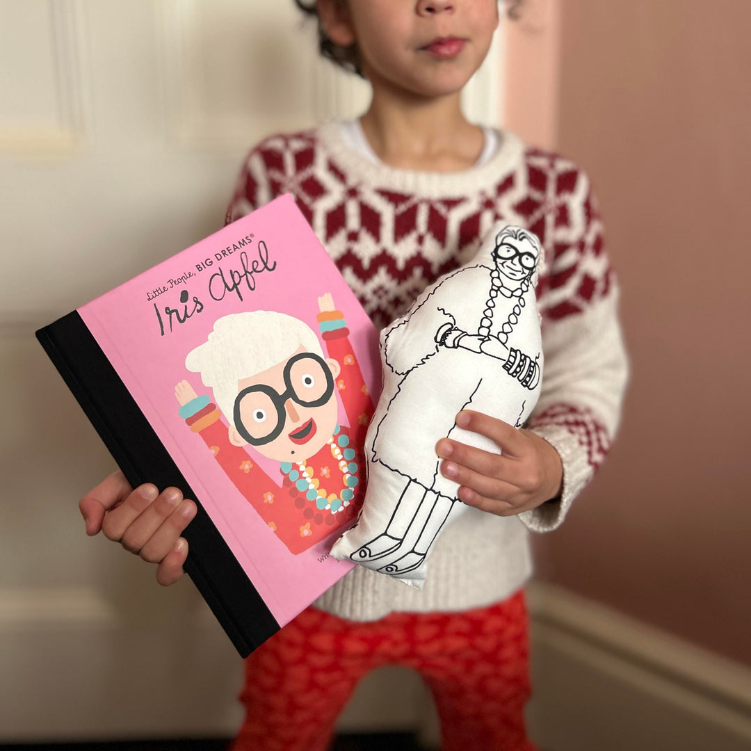 A child holding screen printed doll cushion and Little People Big Dreams book about Iris Apfel's life