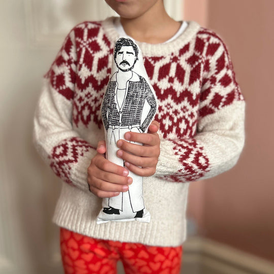 A child holding a black and white screen printed cushion doll depicting an illustration of Pedro Pascal.