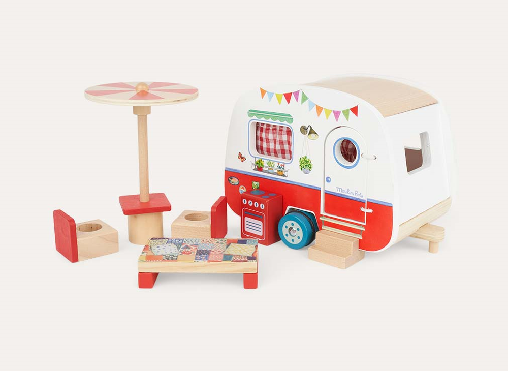 Toy camper with furniture outside, a table and chair set with an umbrealla, a wooden bed and wooden cooker