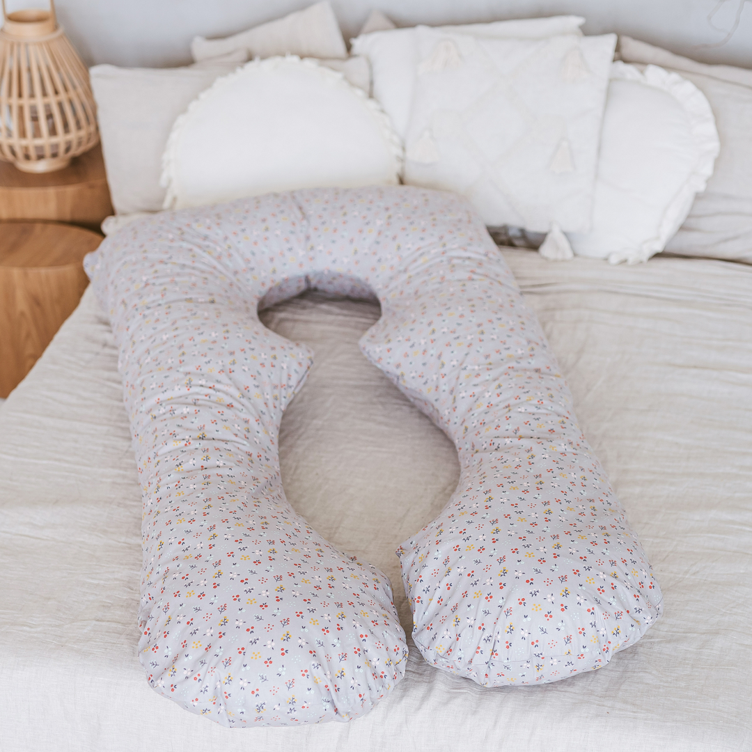 Floral-patterned U-shaped body pillow on a bed with white pillows and bedding.
