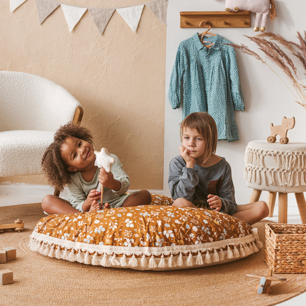 Two children sitting on a brown and white floral floor cushion in a play room