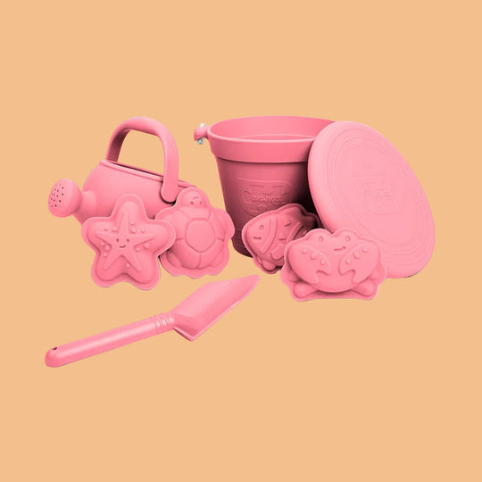 Pink sand toys including a watering can, bucket, and molds on a white background