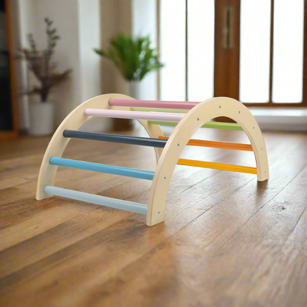 A colourful wooden climbing arch with multicoloured rungs arranged in an arch shape, designed for toddler play.