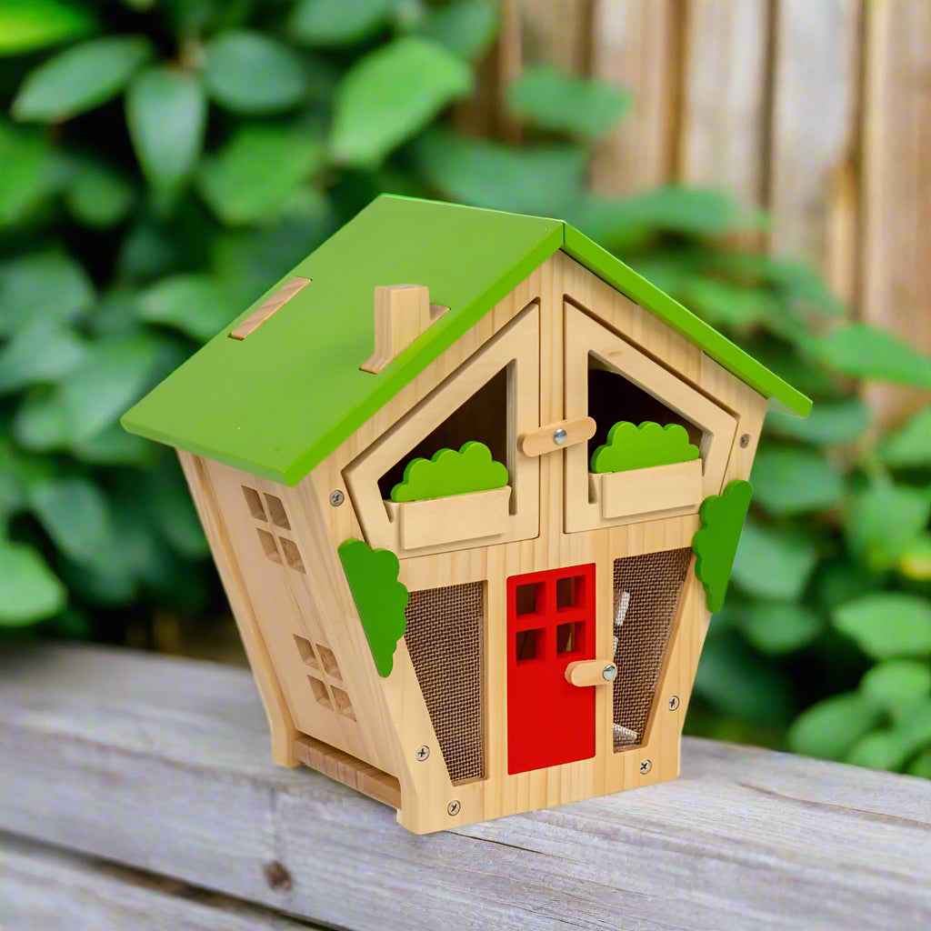 Children's wooden bug house with a green roof, red door, and decorative greenery.