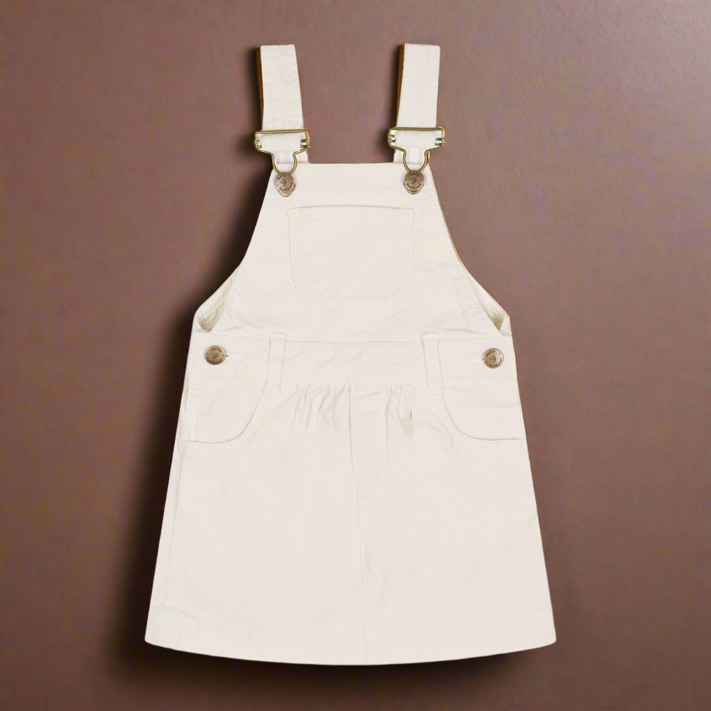 White corduroy dress with two pockets either side of the dress and also a central pocket on the chest, and brass buttons 