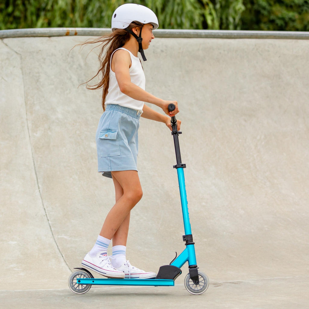 Child riding a scooter wearing a helmet in a skate park