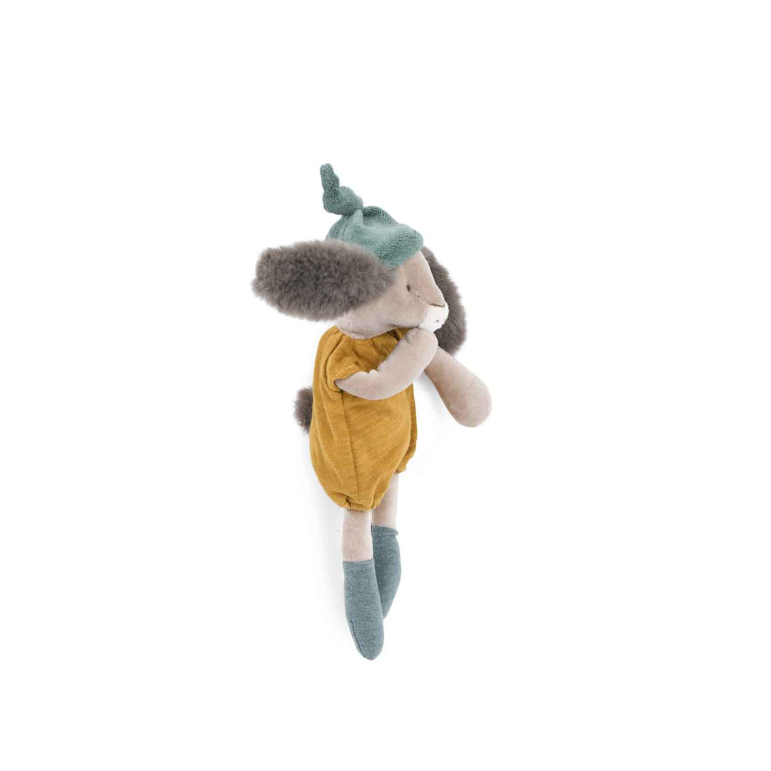 Plush toy rabbit facing the side with its hand to its mouth wearing a teal hat and mustard yellow romper outfit