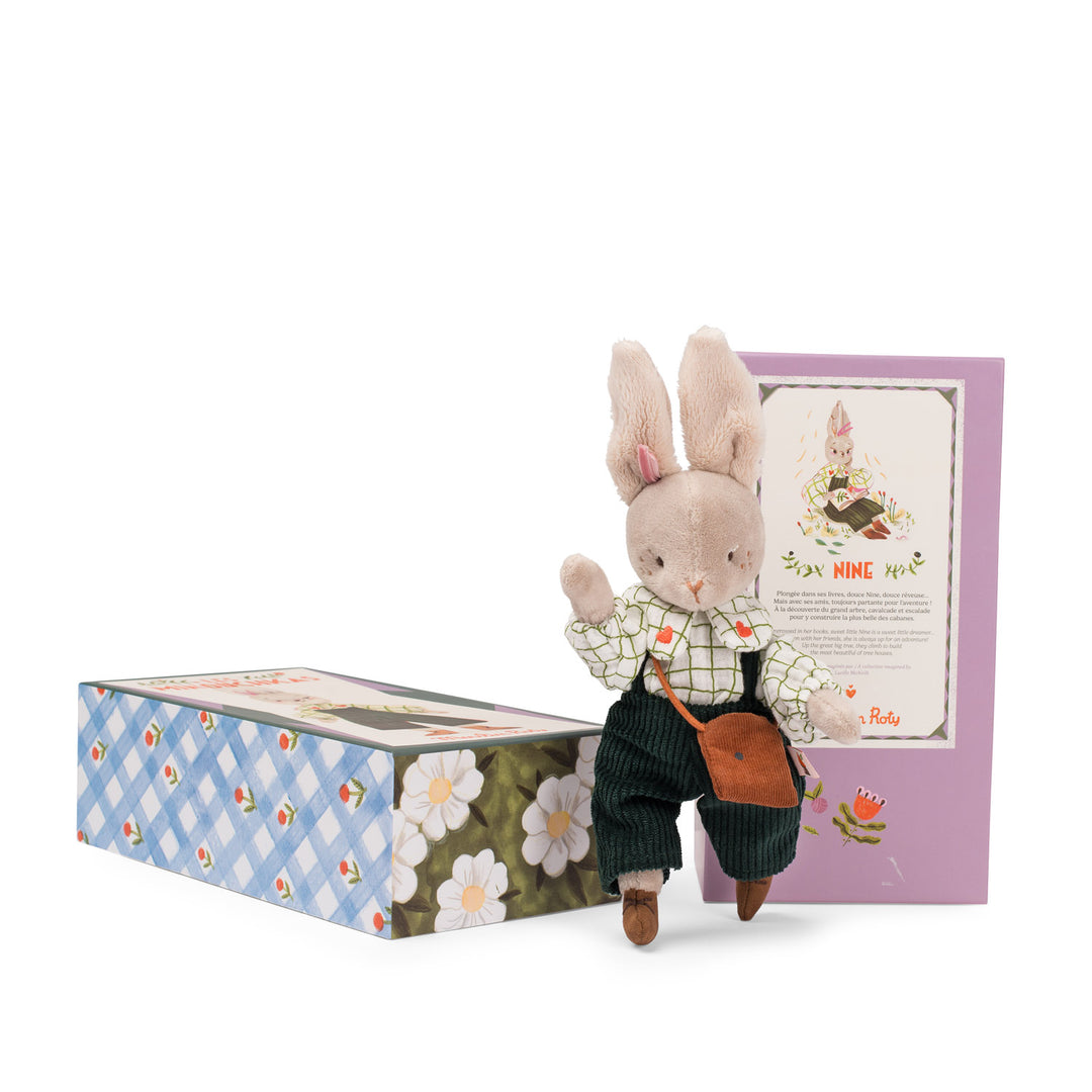 Stuffed rabbit toy with a white checkered shirt and navy corduroy dungarees standing next to a decorative box on a white background