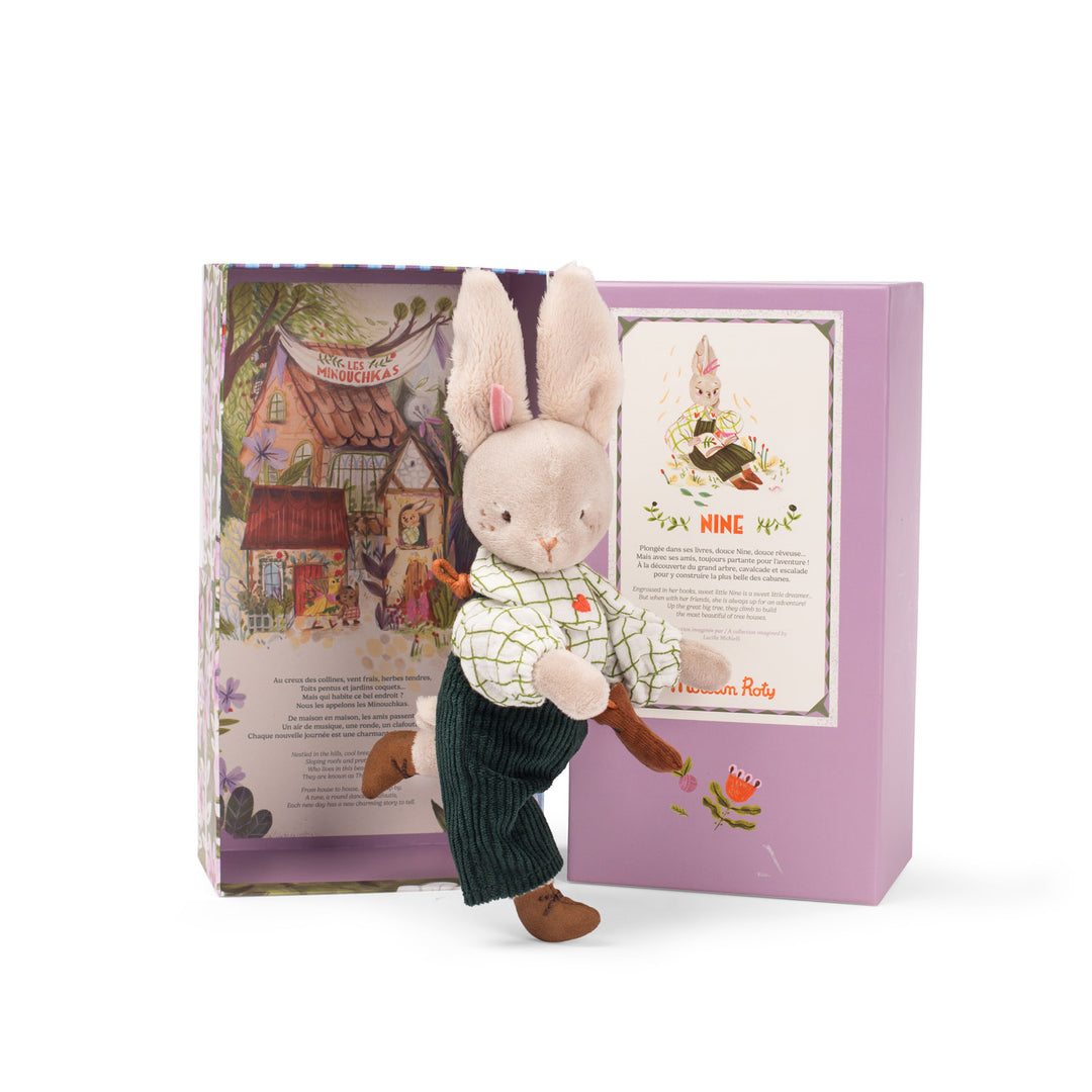 Stuffed rabbit toy with a checkered shirt and corduroy dungarees in front of the decorative box that it comes in