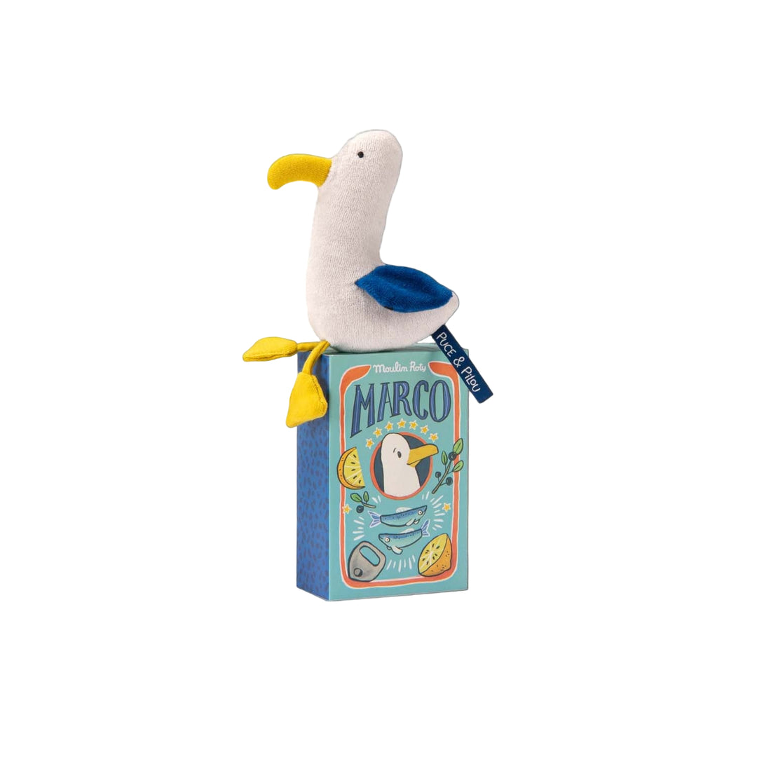 Plush seagull toy rattle with white body, yellow beak and feet and blue wings sitting on its decorative packaging box