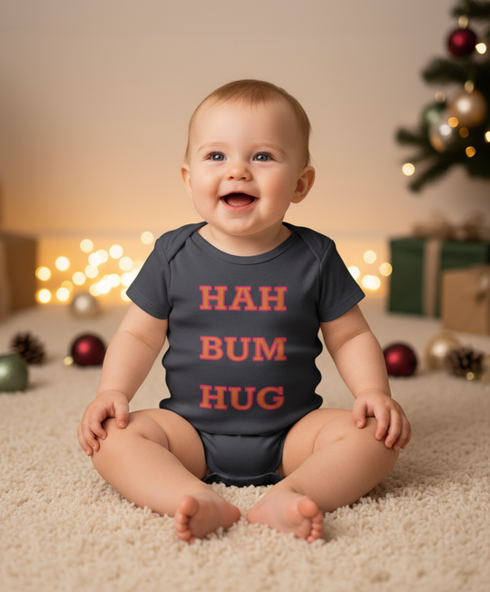 Baby wearing a dark blue onesie with red text sitting on a carpeted floor with Christmas decorations in the background.