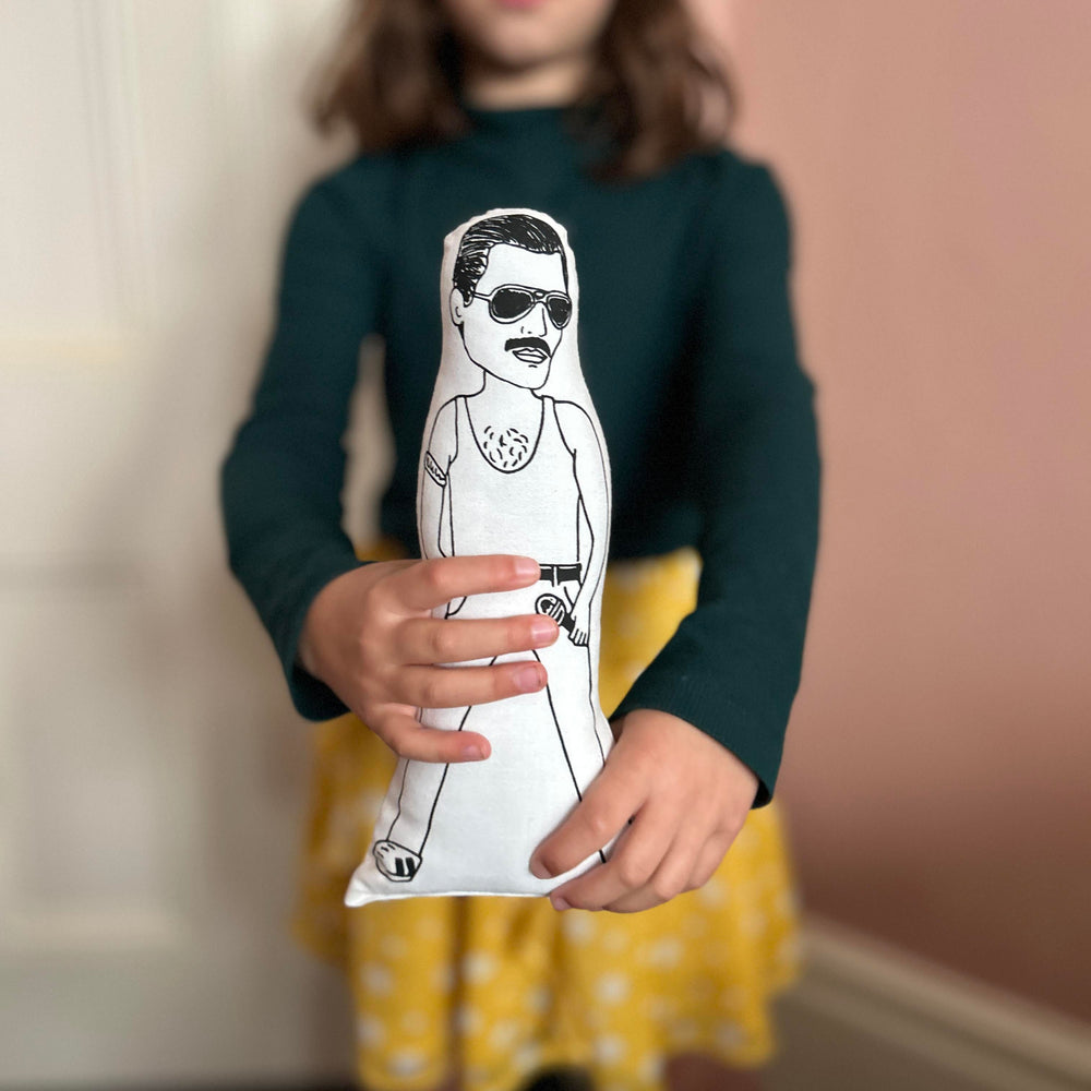 A child holding out a screen printed doll cushion of singer Freddie Mercury towards the camera