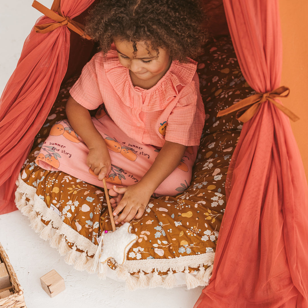 Child sitting on round patterned floor cushion inside a play tent