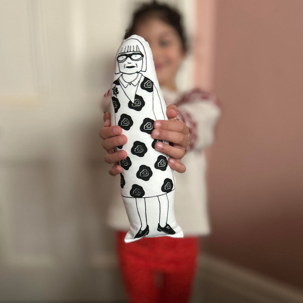 A child holding a black and white screen printed cushion doll depicting a stylised version of Esme Young