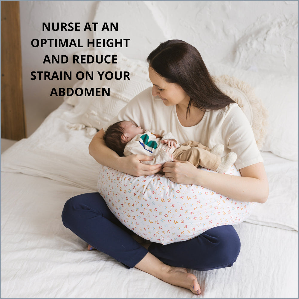 Woman holding a baby in a nursing pillow on a bed with text about nursing a baby at the optimal height to reduce strain on abdomen