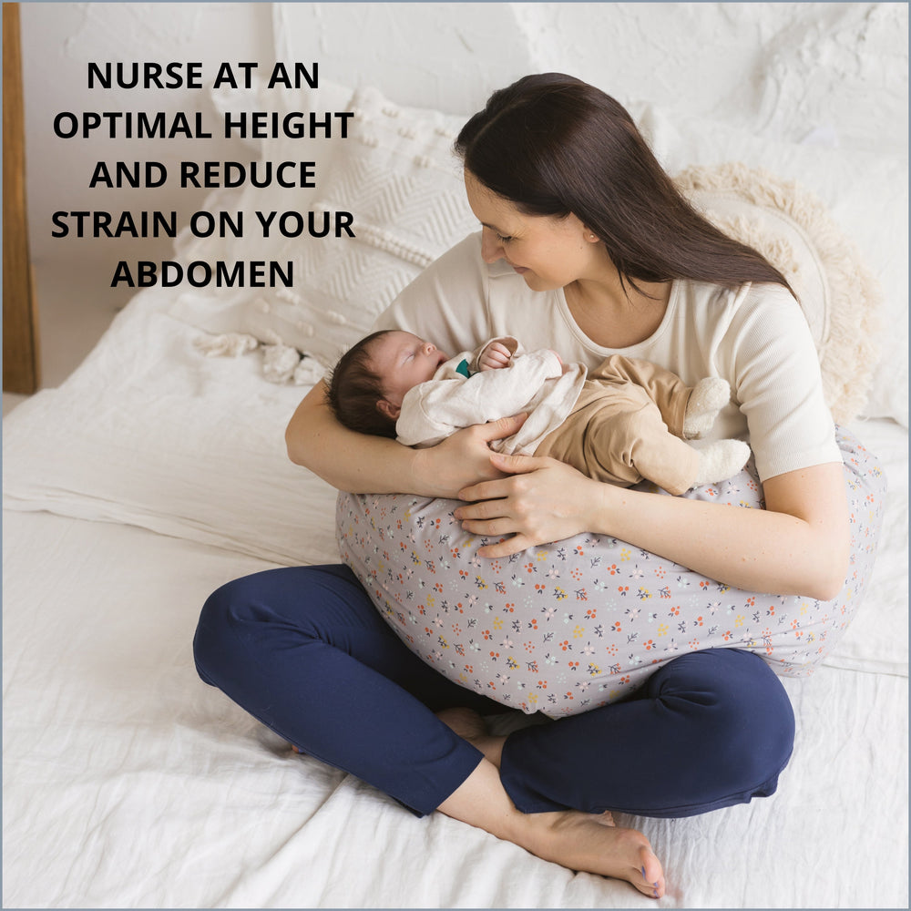 Woman holding a baby in a nursing pillow on a bed, with text saying about nursing a baby at an optimal height to reduce strain on abdomen