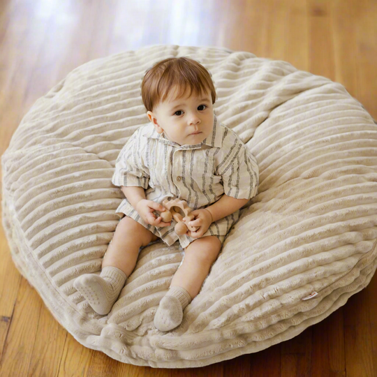 Young child sitting on a large beige textured floor cushion holding a toy