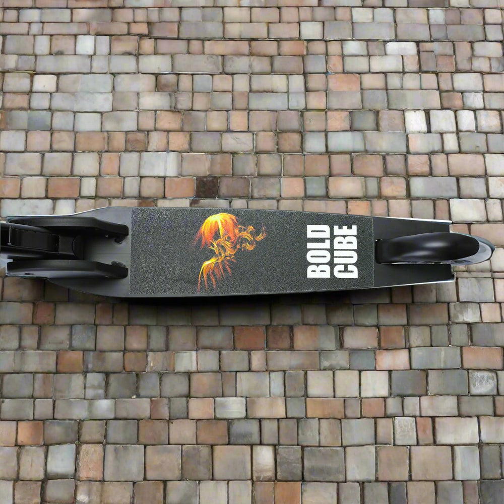 Close up birds eye view looking down at the tread of the scooter, showing a black deck with a fire design and branding 'Bold Cube' written on it