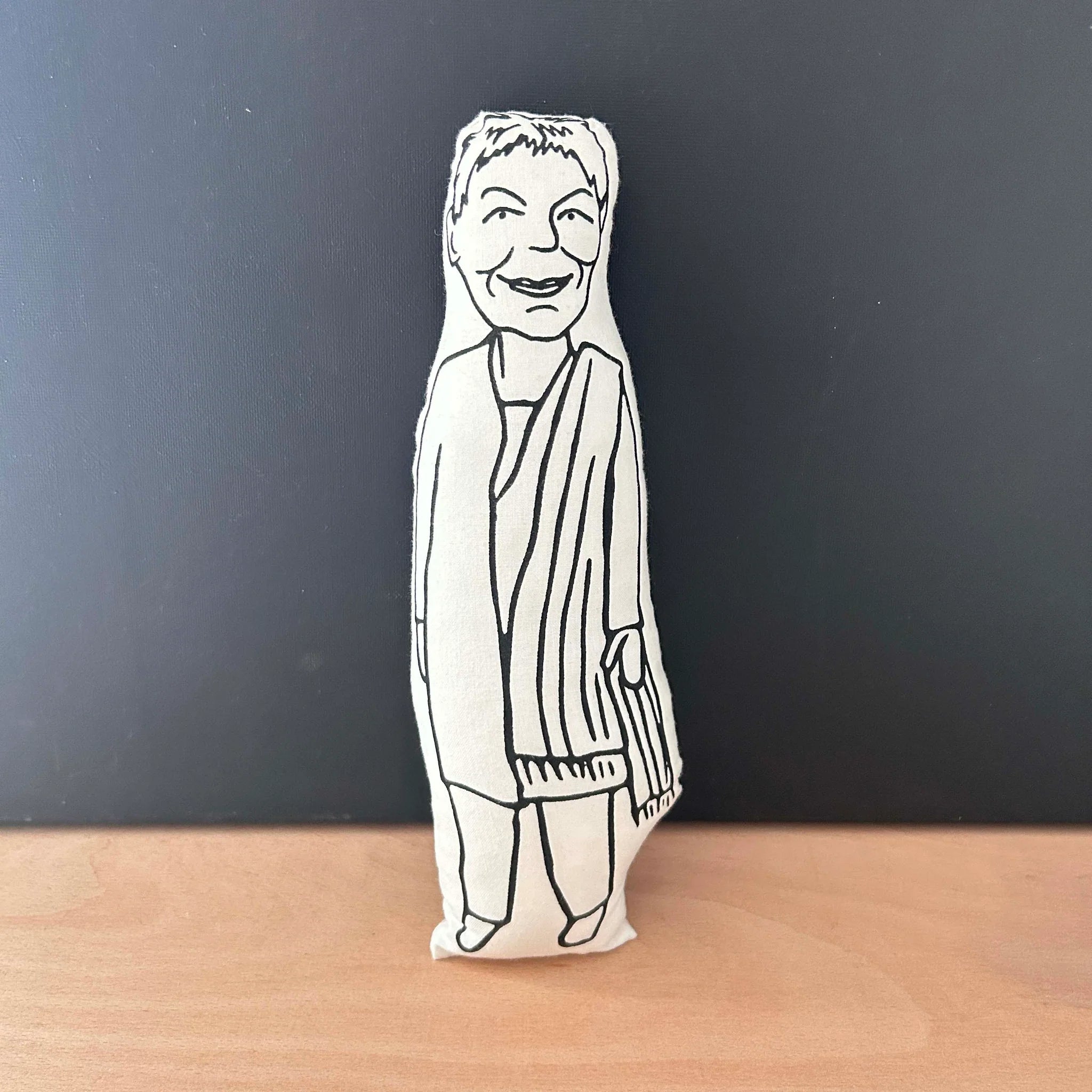 Screen printed dool cushion with white fabric and black illustration depicting stage and screen actress Dame Judi Dench, wearing a loose fitting coat with shawl draped over one shoulder