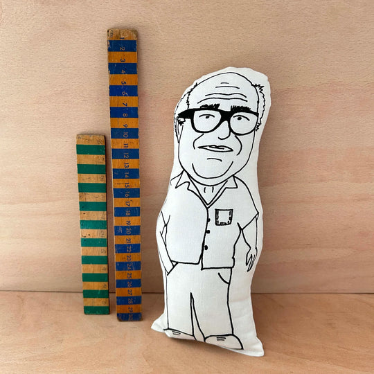 Screen printed doll cushion of Danny DeVito next to two wooden rulers on a wooden background