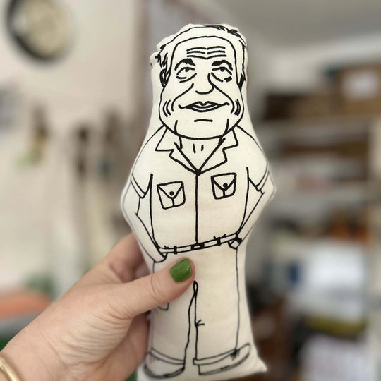 A hand holding up the screen printed doll cushion of David Attenborough with a blurred background