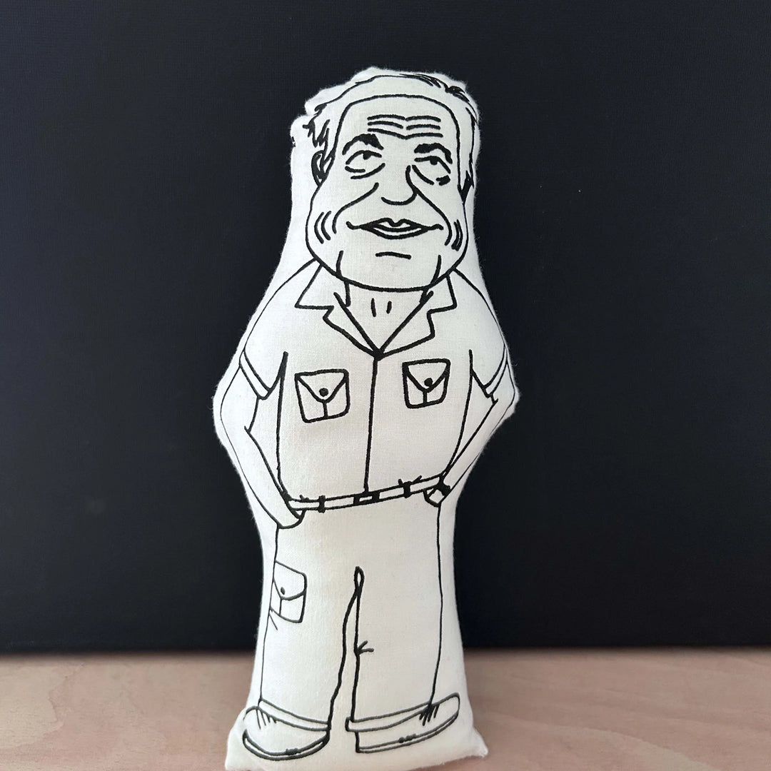 Screen printed doll cushion with white fabric and black illustration depicting nature documentary maker David Attenborough wearing combats with his hands in his pockets