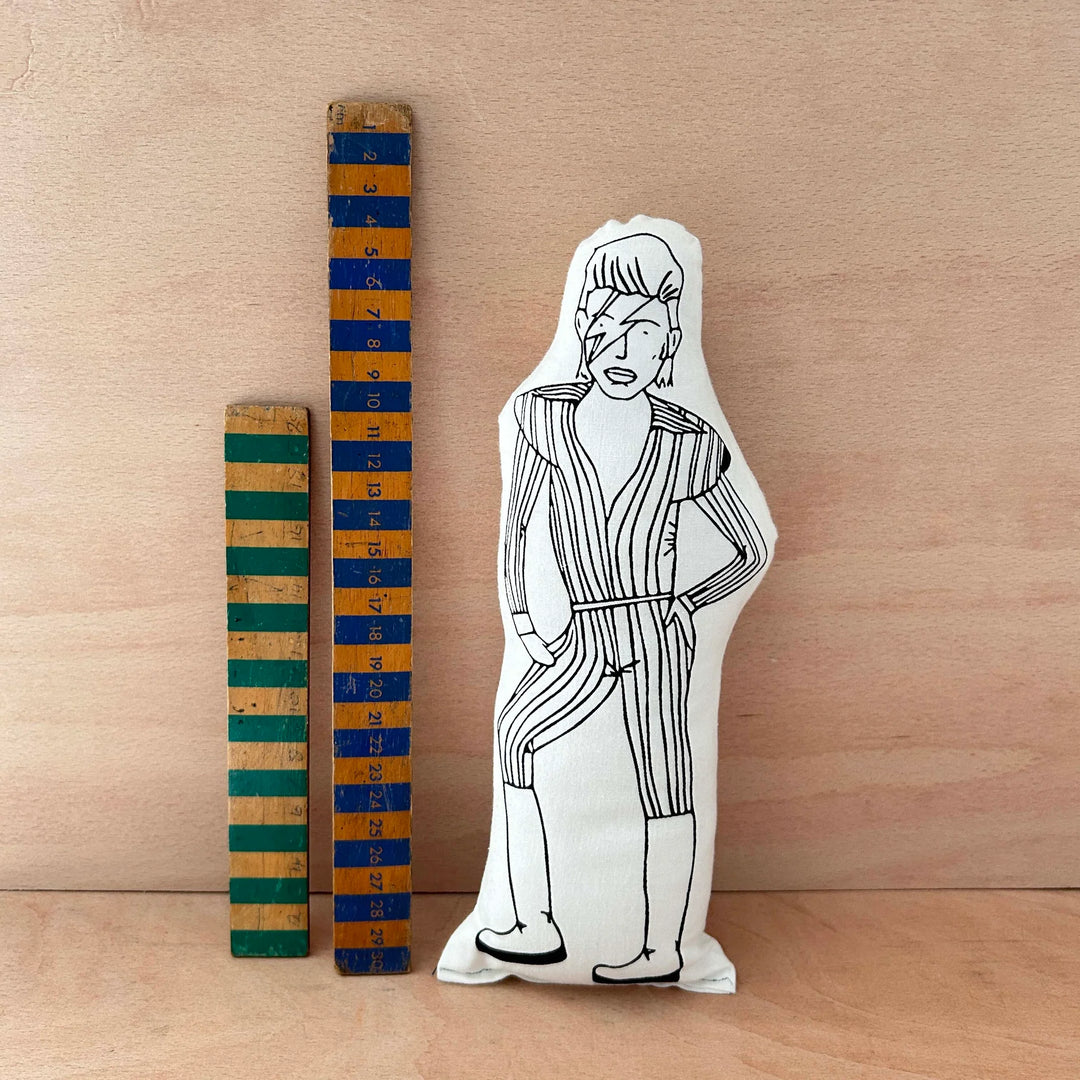 Screen printed doll cushion of David Bowie next to two wooden rulers and a wooden background