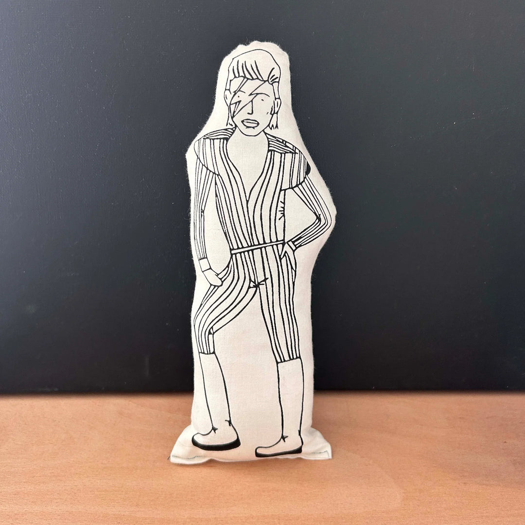 Screen printed doll cushion with white fabric and black illustrastion depicting musician David Bowie in his iconic Ziggy Stardust outfit - a striped suit, big boots and a lightning bolt across the face