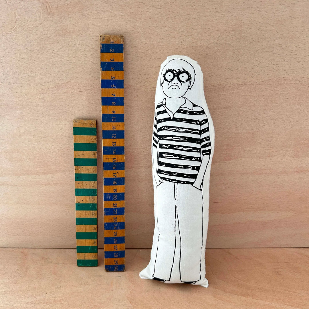 Screen printed doll cushion of David Hockney next to two wooden rulers on a wooden background