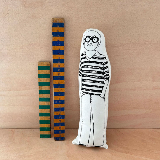 Screen printed doll cushion of David Hockney next to two wooden rulers on a wooden background